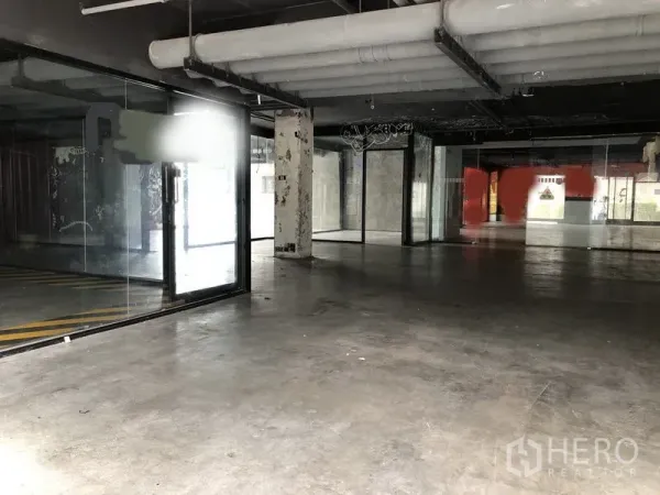 零售空间 出租在Khlong Toei, Bangkok - 宽敞的零售内厅，水泥地面、落地玻璃隔断与外露风管。