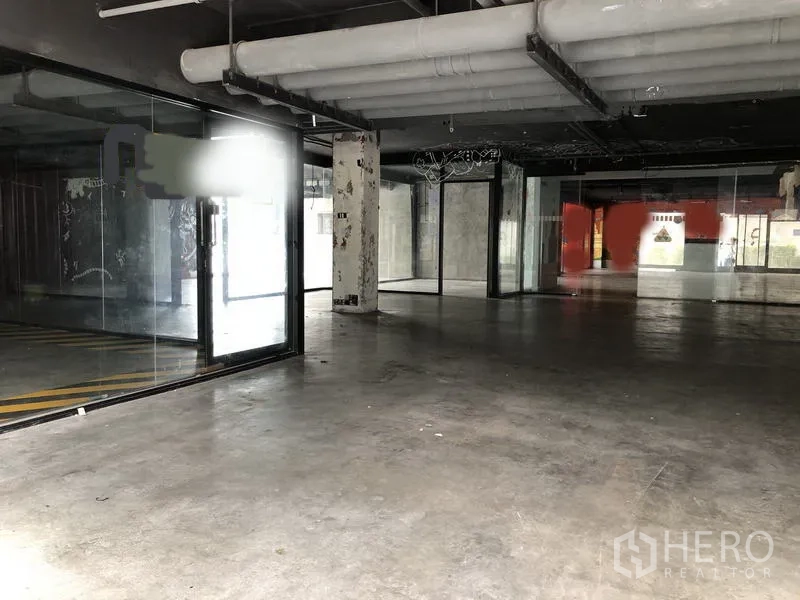 零售空间 出租在Khlong Toei, Bangkok - 宽敞的零售内厅，水泥地面、落地玻璃隔断与外露风管。