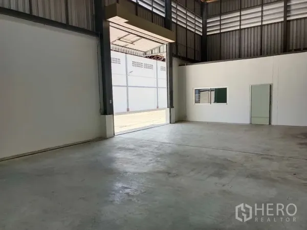 Warehouse for rent in Suan Luang, Bangkok - Spacious warehouse interior with high steel ceiling, polished concrete floor, wide roller shutter opening, and internal office window.