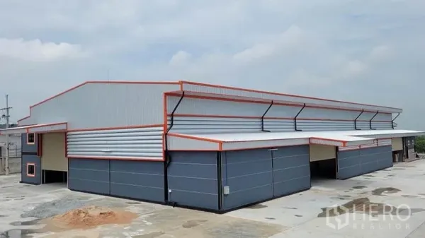 工厂 出租或出售在Phanat Nikhom, Chon Buri - 现代钢结构工厂外观，灰色墙面配橙色收边，多个卷帘门与宽阔混凝土场地。