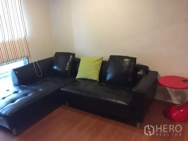 คอนโด ให้เช่าในPhaya Thai, Bangkok - โซฟาหนังสีดำรูปตัวแอลพร้อมหมอนสีเขียวและโต๊ะข้างสีแดง