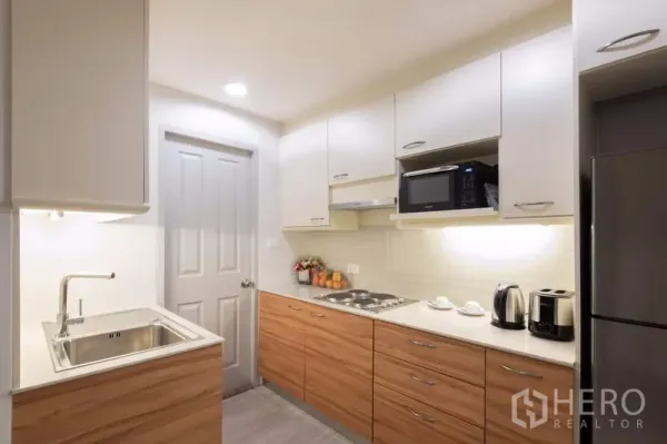 Apartment for rent - Modern closed kitchen with white cabinets, wood lower units, electric cooktop, microwave, kettle and refrigerator.