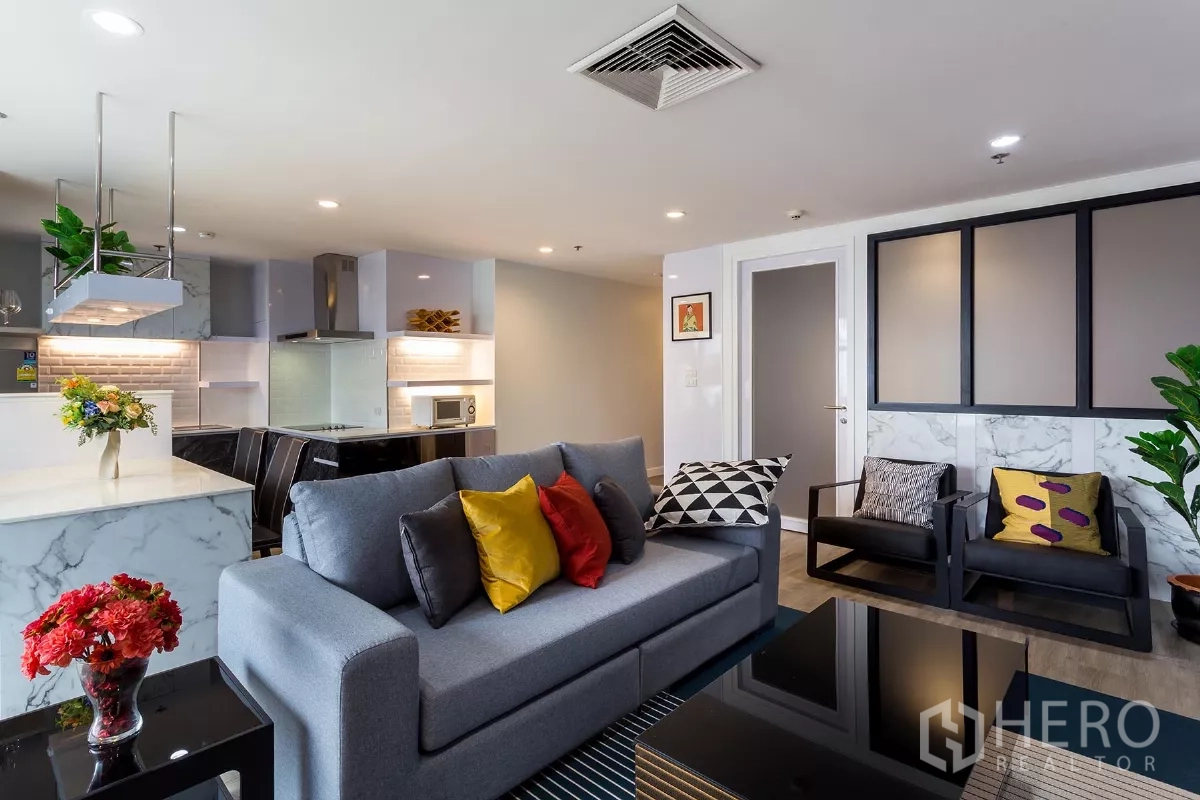 Condominium for rent or sale in Watthana, Bangkok - Cozy lounge with a gray sofa, colorful cushions and a modern kitchen in the background.