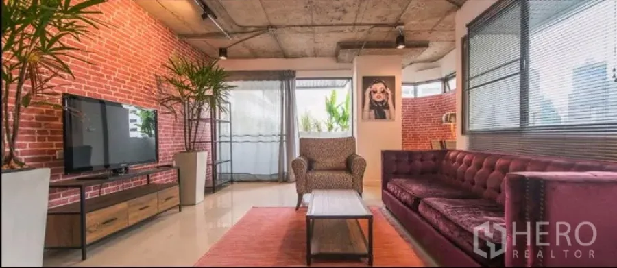 Condominium for rent in Watthana, Bangkok - Loft-style living room with exposed concrete ceiling, brick walls, large windows and a velvet sofa.