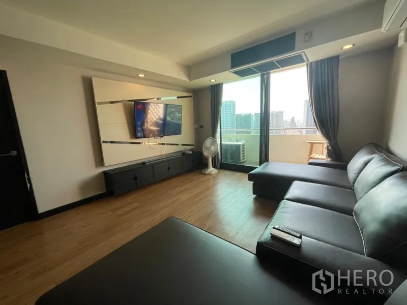 Condominium for sale in Chatuchak, Bangkok - Living room with L-shaped leather sofa, wall-mounted TV and balcony overlooking the skyline.