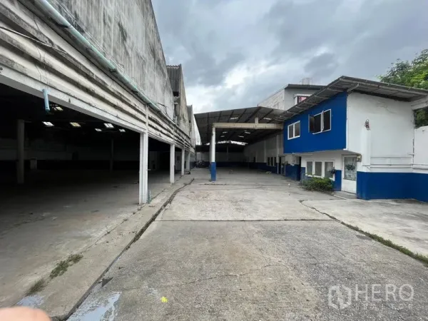 Warehouse for rent in Phra Khanong, Bangkok - Long driveway leading to covered loading bays and a blue-and-white two-storey office.