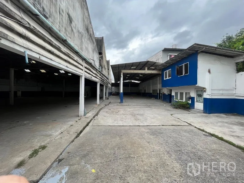 Warehouse for rent in Phra Khanong, Bangkok - Long driveway leading to covered loading bays and a blue-and-white two-storey office.