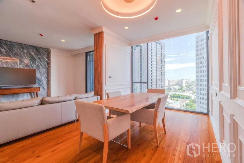Condominium for rent or sale - Dining space with wooden table, upholstered chairs, and floor-to-ceiling corner window.