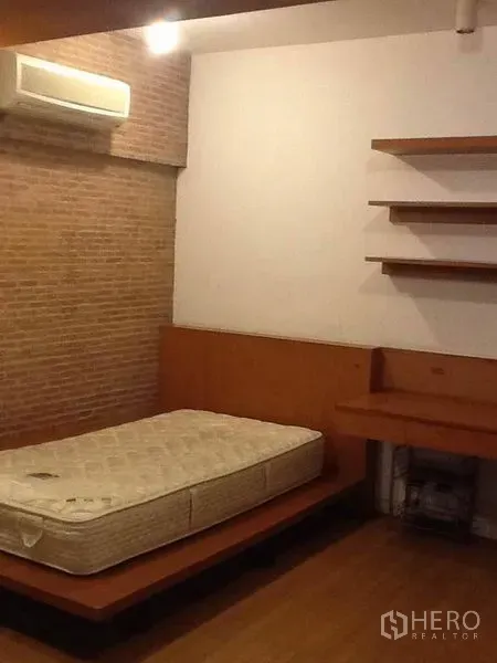 Condominium for rent in Pathum Wan, Bangkok - Bedroom with platform bed, brick accent wall, built-in desk and shelves, and air conditioning.