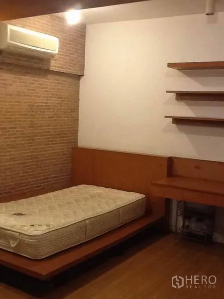 Condominium for rent in Pathum Wan, Bangkok - Bedroom with platform bed, brick accent wall, built-in desk and shelves, and air conditioning.
