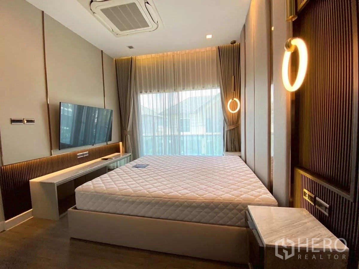 Detached House for rent in Bang Phli, Samut Prakan - Master bedroom with king bed, wall-mounted TV and ring pendant lights by full-height windows.