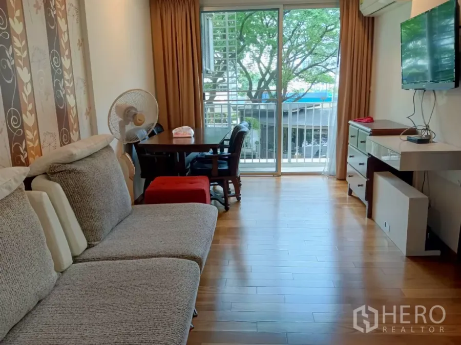 Condominium for sale in Chatuchak, Bangkok - Bright living room with wood flooring, sofa, dining set and sliding glass doors to a balcony with tree views.