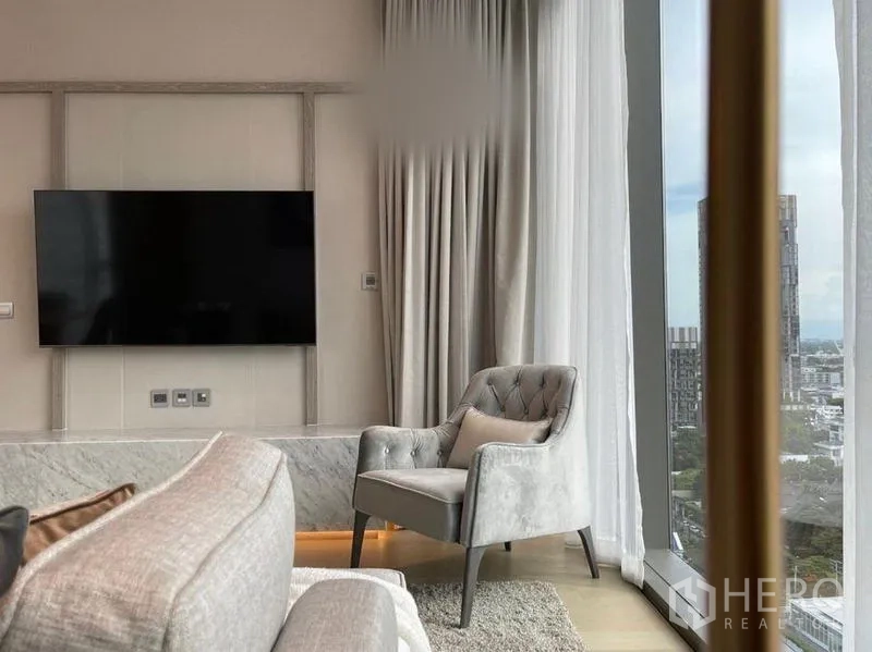 公寓 出租在Watthana, Bangkok - 落地窗旁的休闲单椅，邻近壁挂电视与大理石台面。