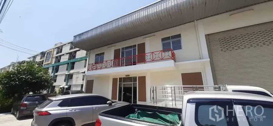 Factory for rent in Bang Sao Thong, Samut Prakan - Renovated factory frontage with red balcony railing, roller shutter door and parking bays.