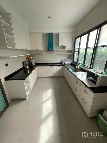 Detached House for sale in Mueang Samut Prakan, Samut Prakan - U-shaped kitchen with white cabinetry, black countertops and large windows.