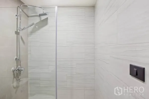 Condominium for rent or sale in Watthana, Bangkok - Glass-enclosed walk-in shower with rain showerhead and light stone tiles in a modern condo bathroom.