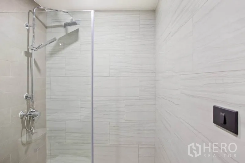 Condominium for rent or sale in Watthana, Bangkok - Glass-enclosed walk-in shower with rain showerhead and light stone tiles in a modern condo bathroom.