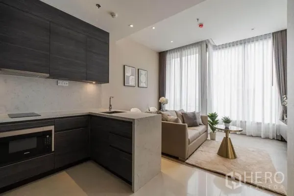 Condominium for rent in Watthana, Bangkok - Modern open-plan kitchen with dark cabinetry flowing into a bright living area with floor-to-ceiling windows.