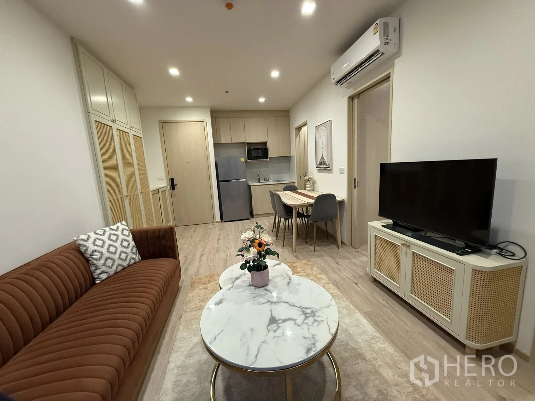 公寓 for rent in Watthana, Bangkok - 客厅朝向厨房，设棕色沙发、大理石茶几、电视柜、餐桌与小巧厨房。