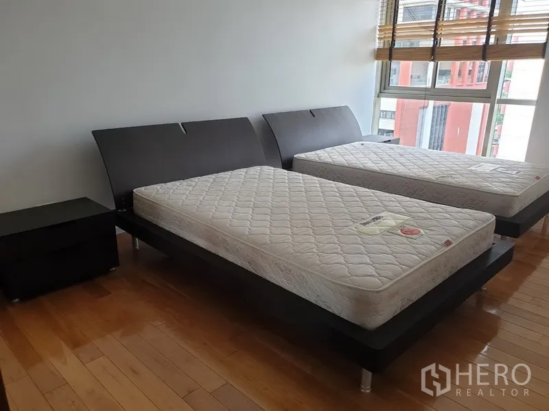 公寓 出租在Bang Rak, Bangkok - 次卧配两张单人床和床头柜，整面窗户俯瞰是隆天际线。