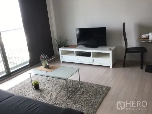 公寓 出租或出售在Watthana, Bangkok - 起居区设有电视柜与玻璃茶几，旁边是通往阳台的大型推拉门。