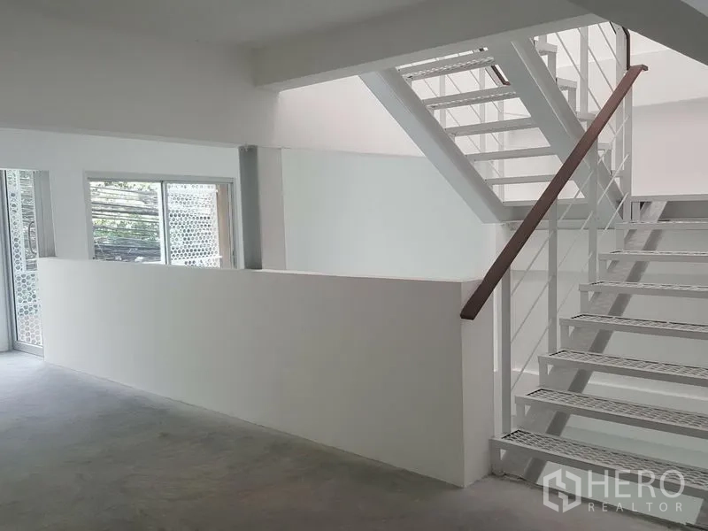 Home Office for rent in Khlong Toei, Bangkok - Close view of a metal staircase with wooden handrail in a light-filled room.