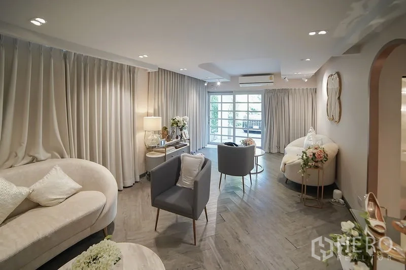 Detached House for rent in Huai Khwang, Bangkok - Cozy lounge with sofas, grey curtains and balcony doors bringing in natural light.