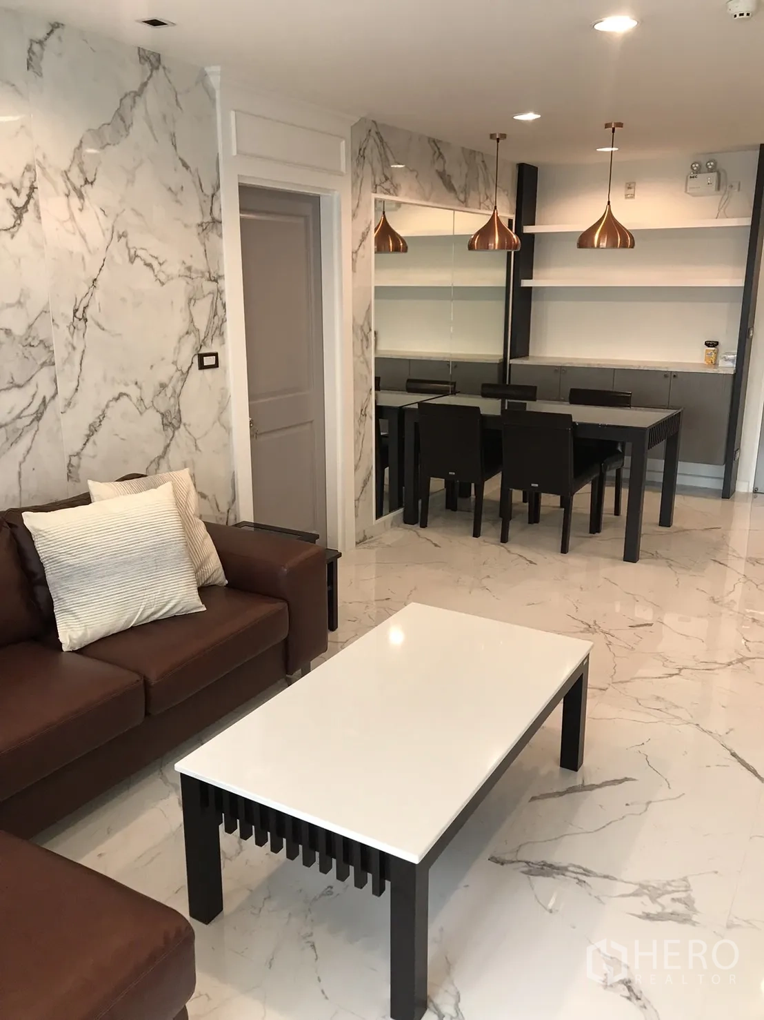 公寓 出租或出售在Khlong Toei, Bangkok - 起居区连通餐区，仿大理石饰面与铜色吊灯。