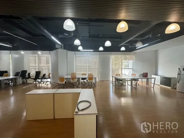 办公空间 出租在Pathum Wan, Bangkok - 开放式办公室，外露天花与吊灯，木地板上摆放多组桌椅及茶水区。