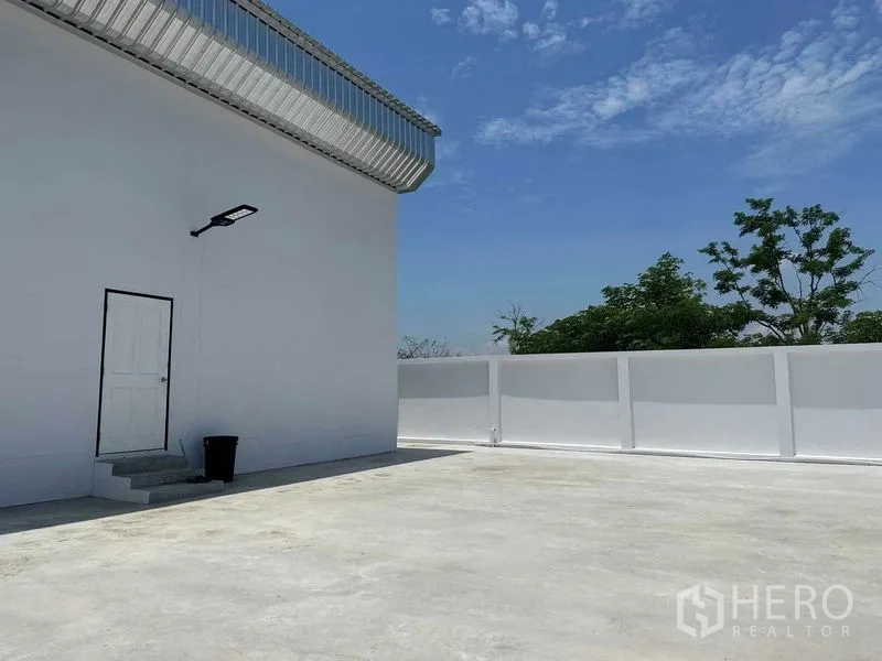 คลังสินค้า ขายในKhlong Luang, Pathum Thani - มุมหลังอาคารใกล้กำแพงสีขาว เห็นประตูบริการและท้องฟ้าแจ่มใส