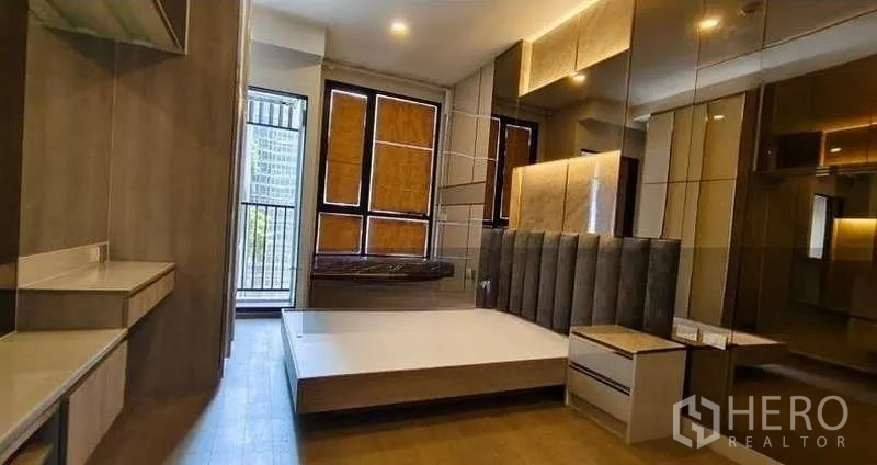 Condominium for sale - Bright bedroom with large windows, balcony access, built-in desk and wood flooring in a Ratchathewi condo.