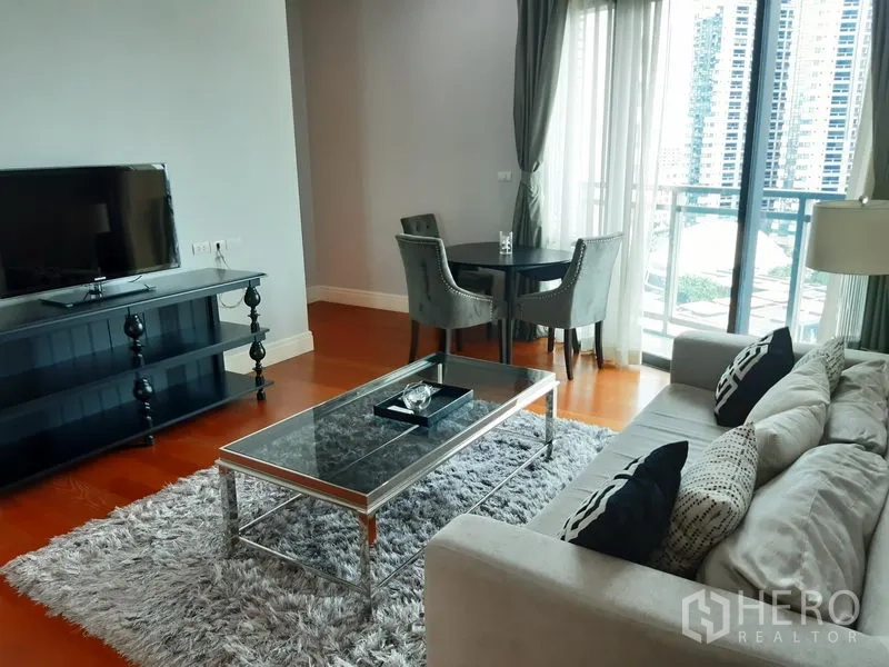 คอนโด ให้เช่าหรือขายในKhlong Toei, Bangkok - ห้องนั่งเล่นพร้อมชั้นวางทีวี ชุดโต๊ะอาหารกลมใกล้ระเบียง มองเห็นวิวสกายไลน์