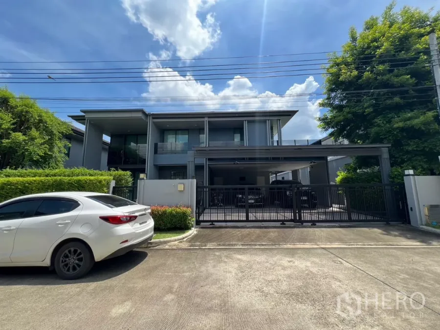 Detached House for rent or sale in Bang Kapi, Bangkok - Modern two-storey detached house with gated driveway and carport, front view under blue sky.