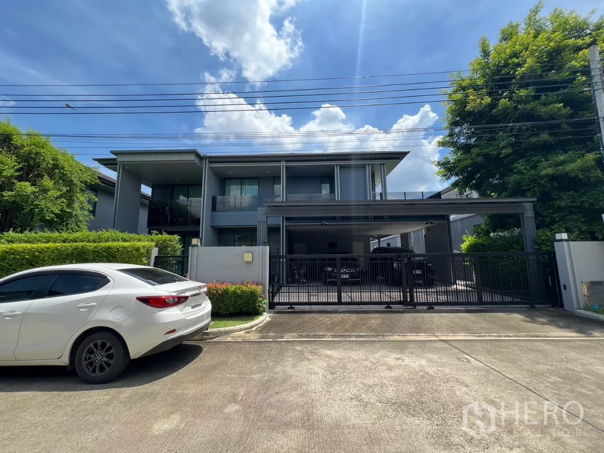 Detached House for rent or sale in Bang Kapi, Bangkok - Modern two-storey detached house with gated driveway and carport, front view under blue sky.