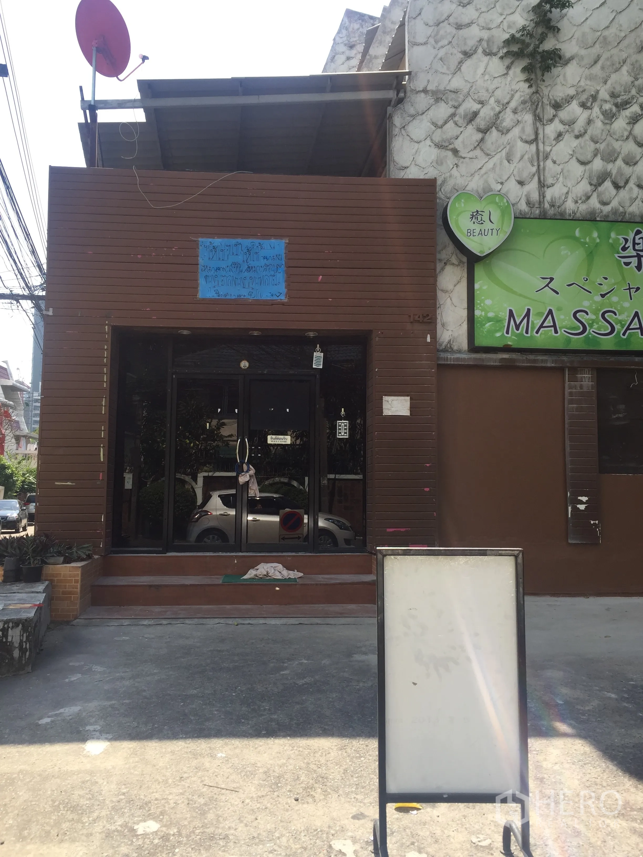 零售空间 出租在Watthana, Bangkok - 临街零售店面，棕色外立面与玻璃双开门，台阶与空白招牌，门前可停车。