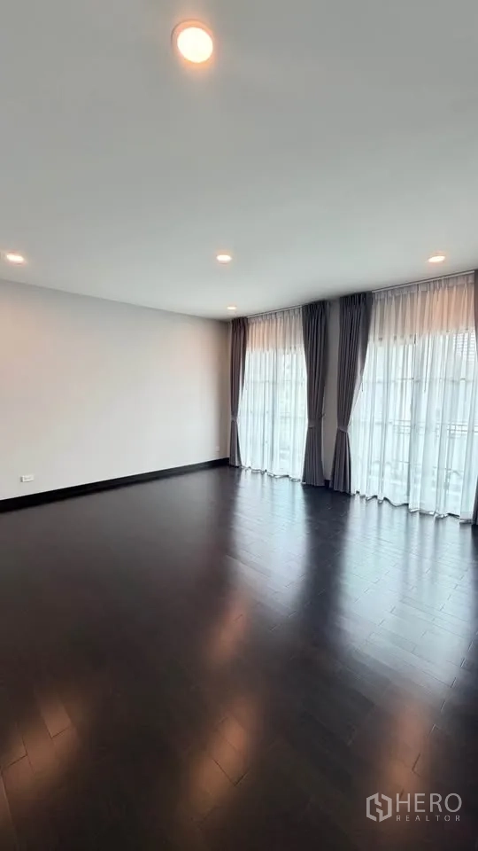 Detached House for rent in Bang Phli, Samut Prakan - Corner bedroom with dark wood floors and large windows dressed with drapes.