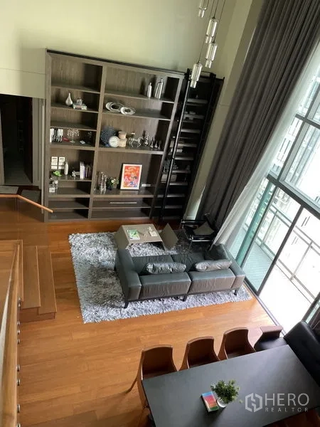 คอนโด ให้เช่าในKhlong Toei, Bangkok - ห้องนั่งเล่นโอเพ่นสเปซ ชั้นวางหนังสือสูงพร้อมบันได โซฟาบนพรม และหน้าต่างกระจกบานใหญ่