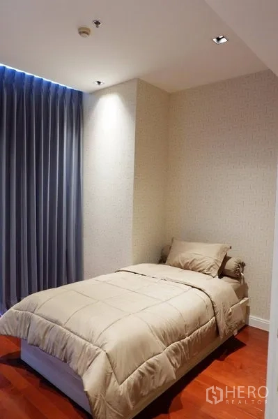 Condominium for rent in Pathum Wan, Bangkok - Cozy second bedroom with single bed, blue blackout curtains and wood flooring.