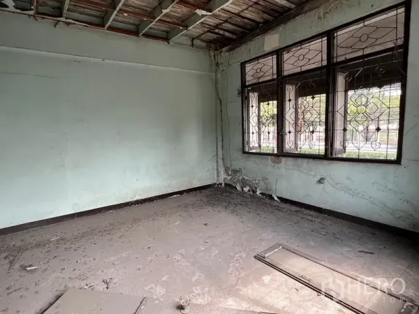 Shophouse for rent or sale in Bang Khen, Bangkok - Vacant room with barred windows, peeling paint and exposed ceiling structure.