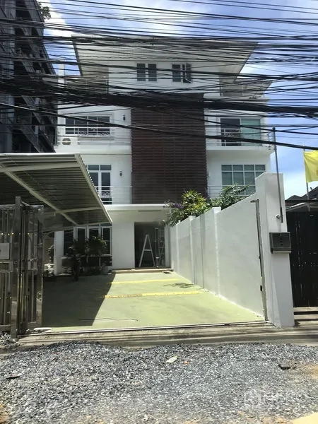 Home Office for rent or sale in Watthana, Bangkok - Modern four-storey home office exterior with gated driveway, covered parking, balconies, and landscaping.
