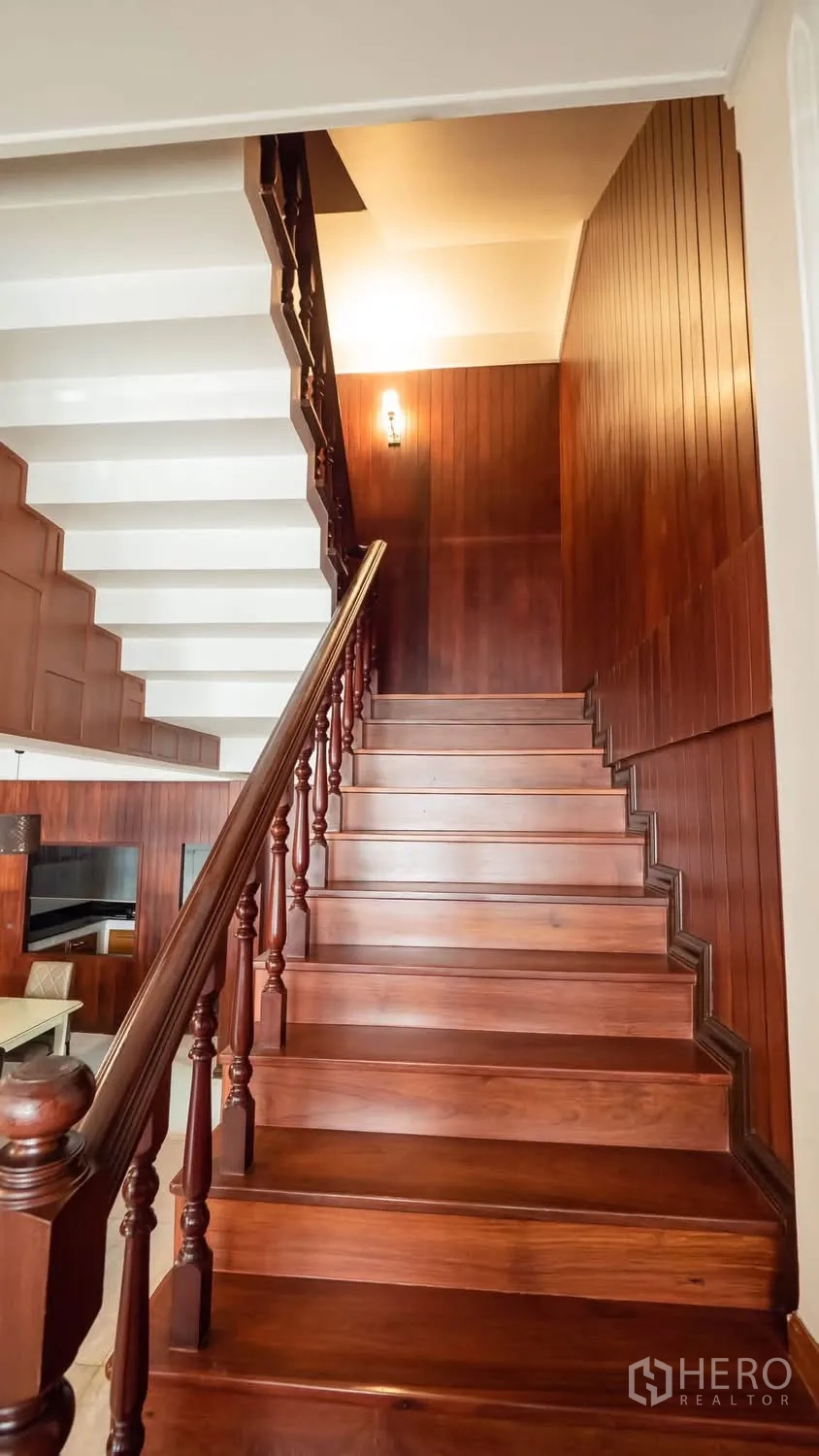 Townhouse for rent in Watthana, Bangkok - Polished hardwood staircase with carved balustrade and wood wall panels.