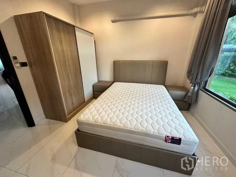 บ้าน ให้เช่าในLat Krabang, Bangkok - ห้องนอนชั้นล่าง เตียงบุหนัง ตู้เสื้อผ้า และหน้าต่างมุมสวน