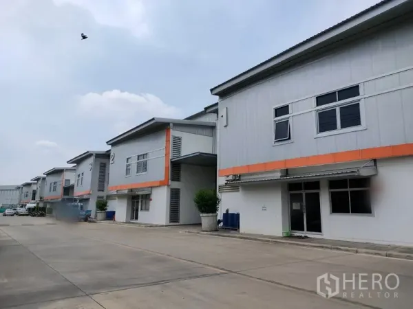 工厂 出租在Phra Nakhon Si Ayutthaya - 工业园内一排现代化厂房，橙色线条点缀，车道宽阔便于通行。