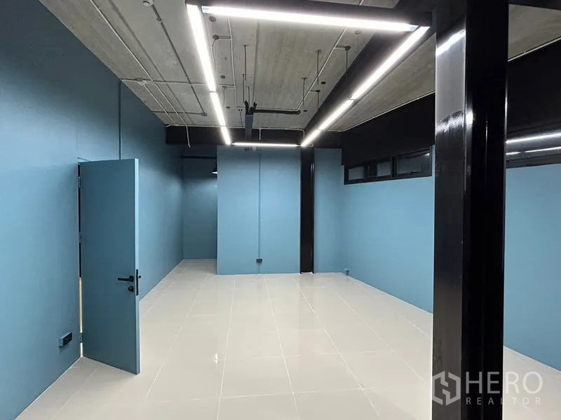 办公空间 出租在Chatuchak, Bangkok - 长形工作空间，蓝色墙面、黑色梁柱、悬挂式线性灯与光洁瓷砖地。