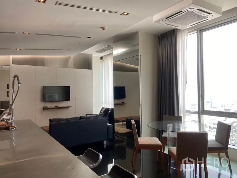 公寓 出租在Sathon, Bangkok - 餐区设圆形玻璃餐桌，临近大窗，连通厨房与客厅。