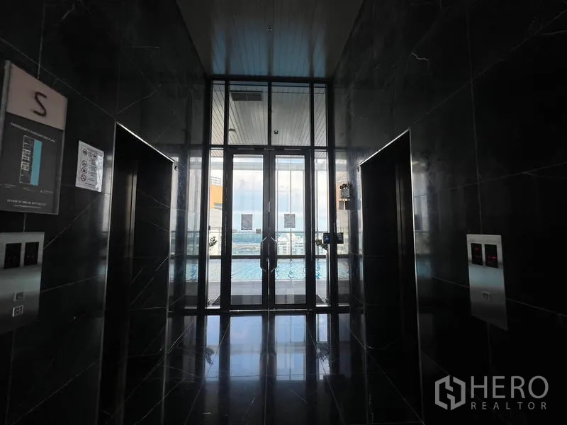 คอนโด ขาย - โถงลิฟต์ผนังหินอ่อนสีดำ ประตูกระจกเปิดสู่สระว่ายน้ำ