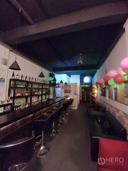 店屋 出租在Khlong Toei, Bangkok - 酒瓶架、长吧台与沙发座，在深色天花灯下。