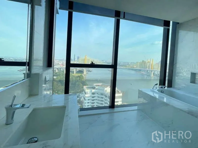 Condominium for rent or sale in Bangkok - Marble bathroom with bathtub and large windows framing river skyline.