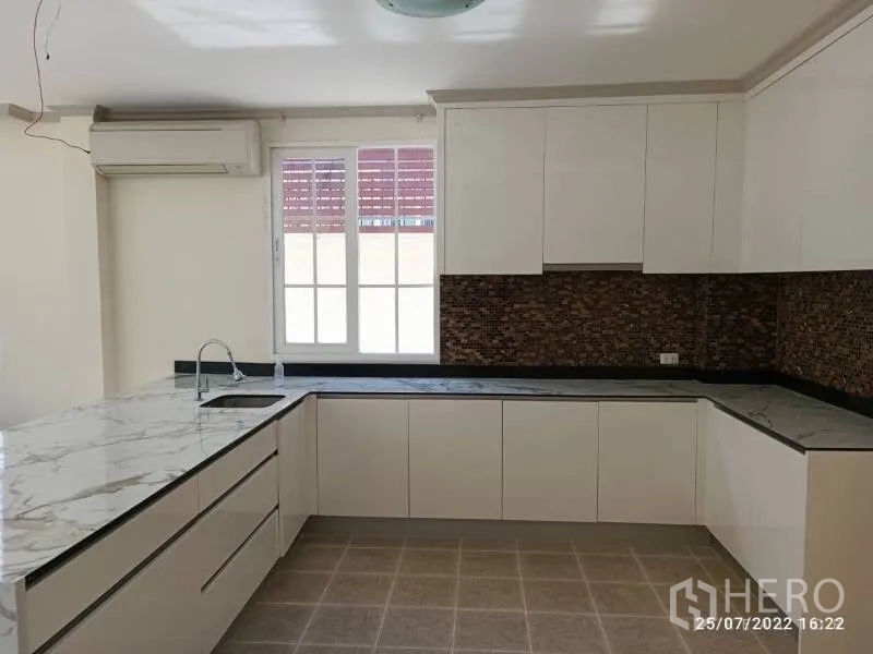 独立式住宅 出售在Prawet, Bangkok - 现代L形厨房，白色柜体与大理石纹台面，采光良好。