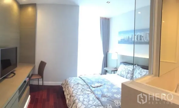 Condominium for rent in Pathum Wan, Bangkok - Cozy guest bedroom with built-in desk, TV console and natural light from a tall window.